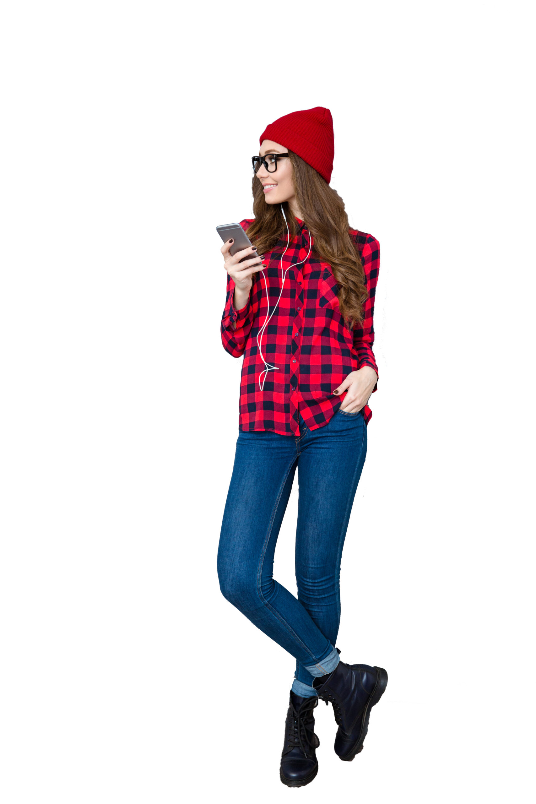 Full length portrait of a hipster woman listening music on smartphone and leaning on gray wall